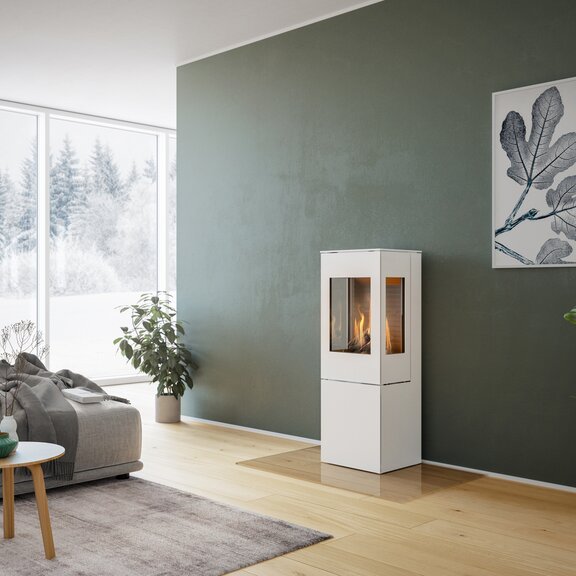 Stufa a gas NEXO 120 in bianco con porta in acciaio e due finestre laterali davanti a una parete verde in un soggiorno decorativo