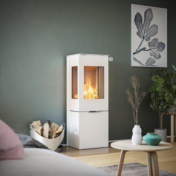 Stufa a legna NEXO 120 in bianco con porta in acciaio e due finestre laterali davanti a una parete verde in un soggiorno decorativo