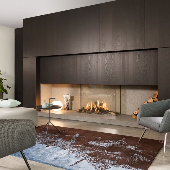 Caminetti a gas GP115/75S vetrati su 3 lati su una parete moderna in legno scuro installata nel soggiorno con divano e poltrona